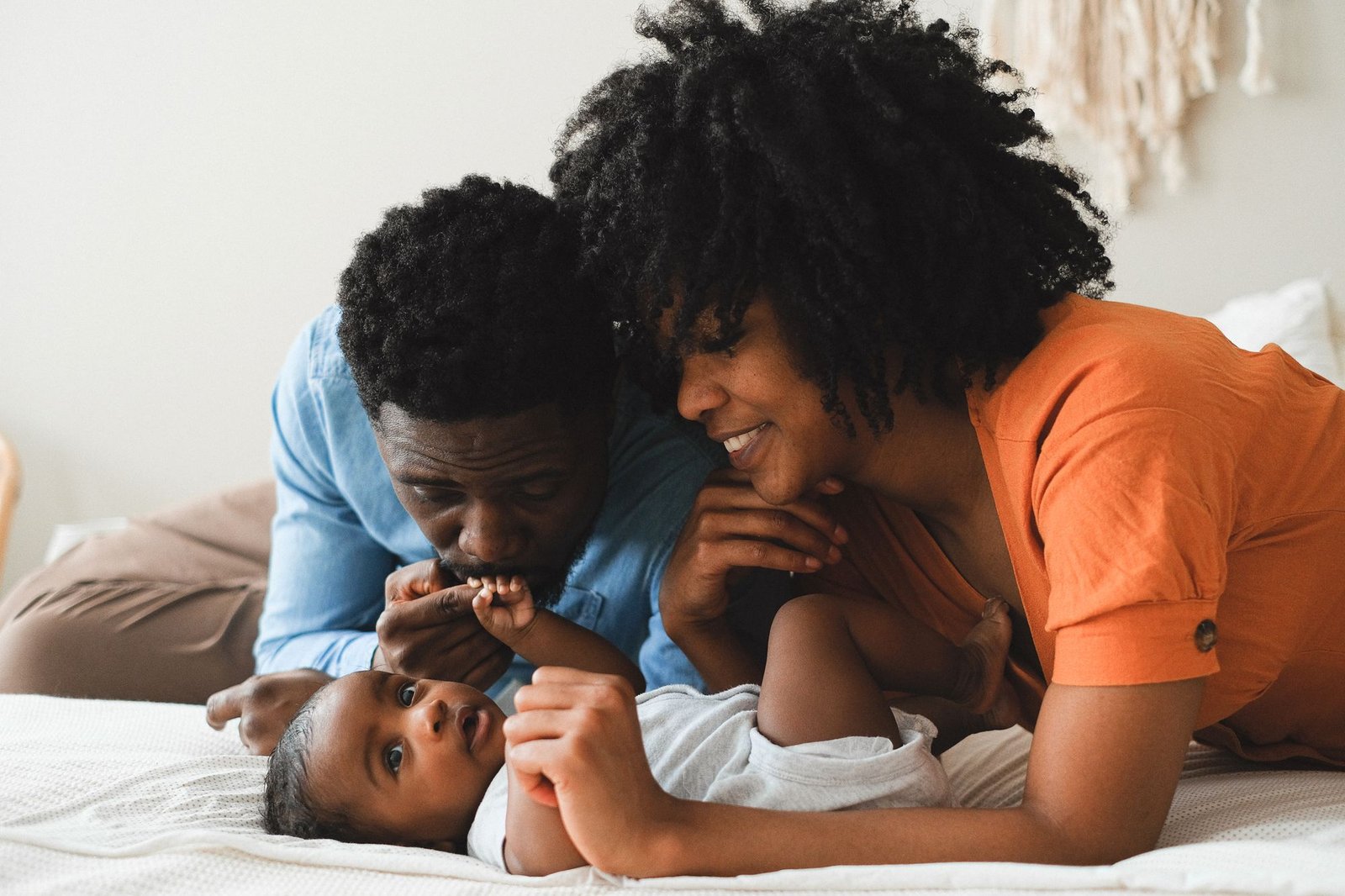 Une maman et un papa jouent avec leur bébé allongé sur le lit